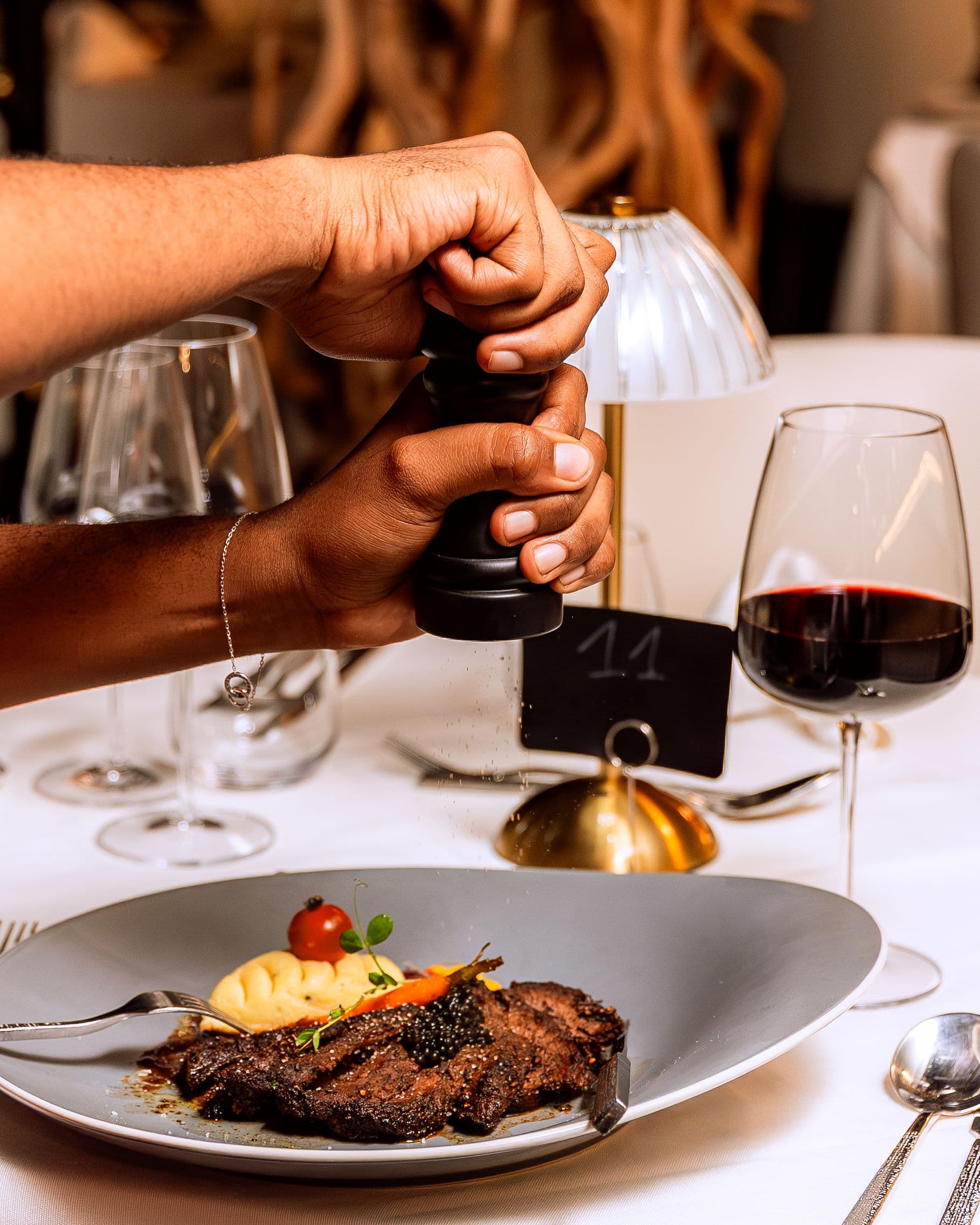 Server seasoning a steak dish tableside with a pepper grinder at Le Youkounkoun
