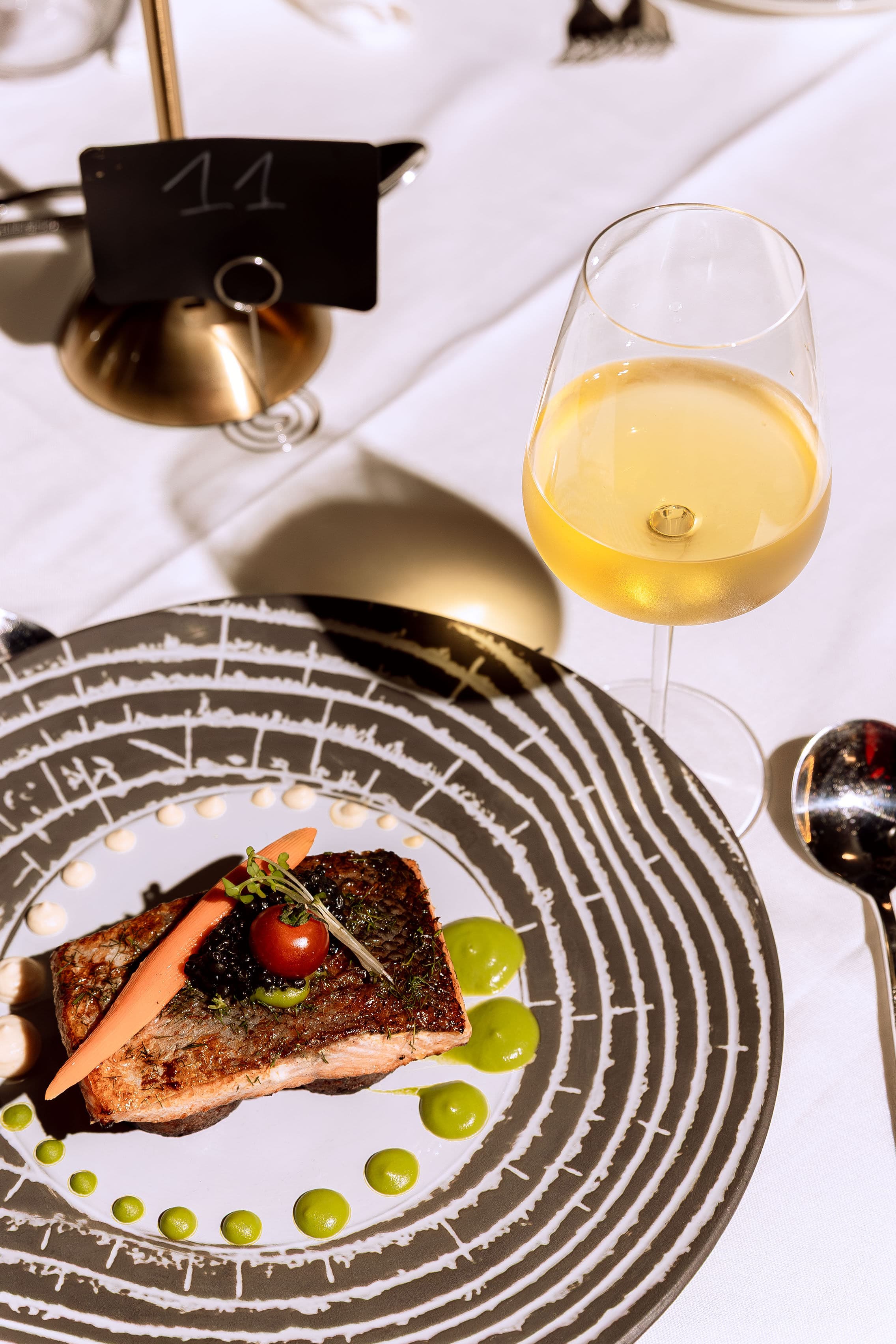Plated fish course beside a glass of white wine at a table set for dinner at Le Youkounkoun